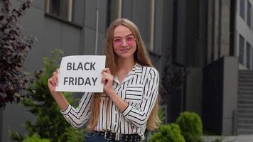 blij tiener meisje tonen zwart vrijdag inscriptie, lachend, op zoek tevreden met laag prijzen video