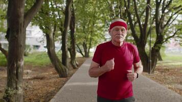 Senior old man running, working out cardio in park and using bluetooth earphones, listening music video