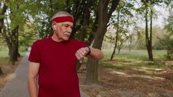 Senior old man running in park and using smart watch, tracking result after fitness workout video