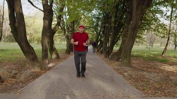 anziano vecchio uomo in esecuzione nel parco e utilizzando inteligente guarda, puntamento risultato durante fitness allenarsi video