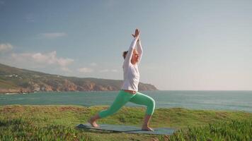 Fit senior woman practicing warrior pose Virabhadrasana on beach video