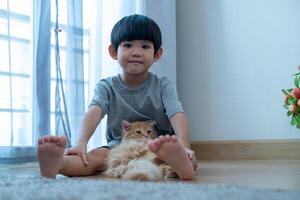 un pequeño asiático chico cariñosamente sostiene un naranja gatito. foto