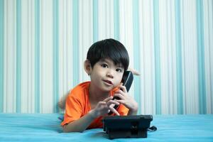 A little Asian boy lies on the bed talking on the phone. photo