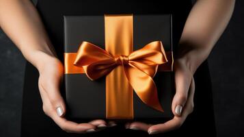 AI generated Woman's hands cradle a black gift box adorned with an orange bow on a dark background. Ai Generated photo