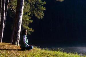 Woman is relaxingly practicing meditation yoga in the forest to attain happiness from inner peace wisdom serenity with beam of sun light for healthy mind wellbeing and wellness soul photo