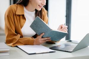 Young woman listening music from headphones and writing note for her work idea in diary book photo