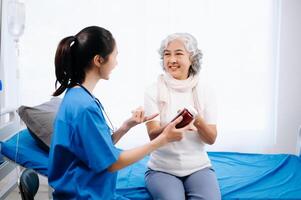 Doctor and Asian elderly patient who lie on the bed while checking pulse, consult and explain with nurse taking note in hospital wards. photo