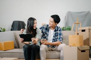 joven Pareja con grande cajas Moviente dentro un nuevo casa, nuevo Departamento para pareja, joven asiático hombre y mujer Ayudar a levantar cajas en sofá foto