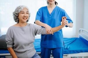 asiático fisioterapeuta Ayudar hembra paciente extensión brazo durante ejercicio correcto con pesa en mano durante formación mano foto