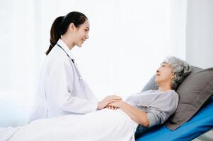 Doctor and Asian elderly patient who lie on the bed while checking pulse, consult and explain with nurse taking note in hospital wards. photo