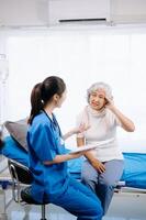 Doctor and Asian elderly patient who lie on the bed while checking pulse, consult and explain with nurse taking note in hospital wards. photo