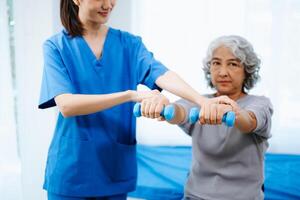 asiático fisioterapeuta Ayudar hembra paciente extensión brazo durante ejercicio correcto con pesa en mano durante formación mano foto