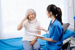 Doctor in white suit take notes while discussing and Asian elderly, woman patient who lying on bed with receiving saline solution photo