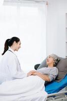 Doctor in white suit take notes while discussing and Asian elderly, woman patient who lying on bed with receiving saline solution photo