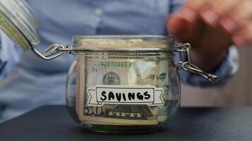 Female hands take money from Saving Money In Glass Jar filled with Dollars banknotes. DONATE transcription in front of jar. Managing personal finances extra income for future insecurity background video