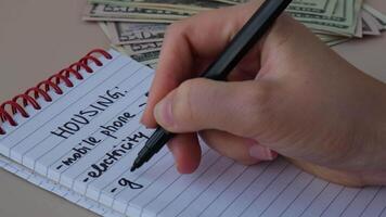 Woman writing in notebook housing expenses. Dollar cash money Counting bills for electricity, gas, water. Concept of Efficient Consumption and Economy. Spending habits video