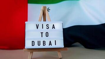 Lightbox with text VISA TO DUBAI on background of waving UAE flag made from silk. United Arab Emirates flag with concept of tourism and traveling. Inviting greeting card, advertisement. Dubai welcoming card video