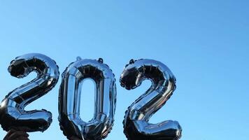 silver- folie siffra 2023 förändra till 2024 firande ny år ballong på blå himmel bakgrund. Lycklig ny år hälsningar begrepp. händer innehav ballonger två tusen tjugotredje förändra till två tusen tjugofjärde år jul Semester 4k antal fot video