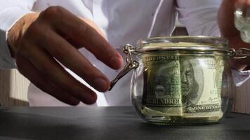 Man hands counting expenses banknotes of dollar cash from glass jar in the piggy bank and count them. Close up of hands unrecognizable Businessman. Save up budget investment concept. American bucks fund savings footage video