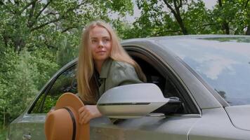 blond kvinna i hatt fastnar huvud ut av vindskydd bil. ung turist utforska lokal- resa framställning uppriktig verklig ögonblick. långsam rörelse Sann känslor uttryck av få bort och refresh koppla av på öppen rena luft video