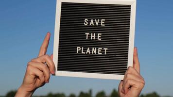 Hands of protester in shape of heart with text SAVE THE PLANET on black board on background of sunflower field. Reuse reduce recycle concept. Protesting for nature Climate strike volunteer protest against earth pollution, global warming video