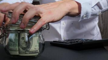 Man hands counting expenses banknotes of dollar cash from glass jar in the piggy bank and count them on calculator. Close up of hands unrecognizable Businessman. Save up budget investment concept. American bucks fund savings footage video