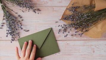 plano deitar composição do fêmea mãos sair em mesa verde envelope com seco lavanda flores cópia de espaço modelo zombar acima. topo visualizar. conceito do Casamento convite cartão postal. o negócio propaganda marca em branco video