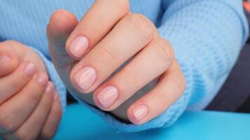 Woman manicured hands, stylish beige nails. Closeup of manicured nails of female hand in blue sweater in blue background. Winter or autumn style of nail design concept. Beauty treatment. video