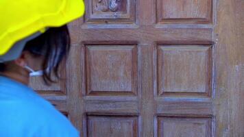 Asian female worker wearing a safety helmet Using sandpaper to polish a wooden door at home. video