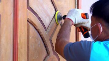 cerca arriba mano de edad mediana asiático hombre usos un madera lijadora a polaco un puerta a hogar. video