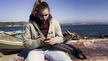 jovem menina é olhando para celular perto a beira-mar video