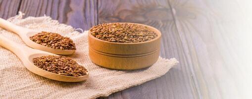 Brown flax seeds or flax seed in a small bowl on sacking and two wooden false on a brown wooden table photo