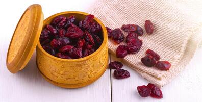 Dried cranberries in a wooden cup with a lid and burlap on a white wooden table photo