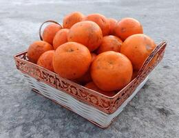 un mimbre cesta lleno de Fresco naranja frutas en el piso foto