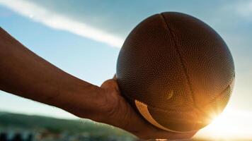 mano sostiene americano fútbol americano pelota a puesta de sol foto
