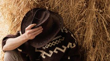 Tired cowboy leaning on hay bale photo