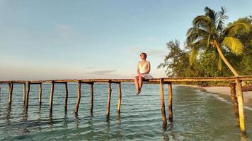 sereno tropical ajuste con un persona meditando en un de madera muelle a atardecer, evocando conceptos de paz, consciencia, y vacaciones escapar video