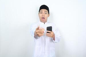 shocked asian muslim man pointing forward to camera with holding mobile phone photo