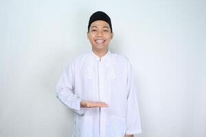 attractive muslim asian man presenting hand to the middle with smiling face isolated on white background, looking at camera photo