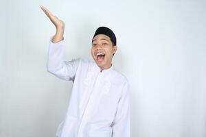 cheerful muslim asian man screaming while raising hand to presenting empty space above isolated on white background photo