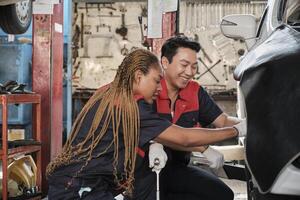 Professional male automotive supervisor trained Black female mechanic technician to screw car wheel nuts for repair at garage, vehicle maintenance service works industry occupation business jobs. photo