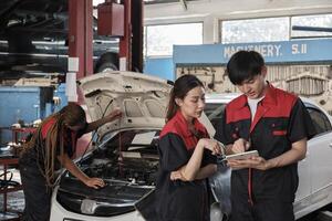 Two Asian professional mechanics, male supervisor engineer, and partner discuss and inspect repair work checklists at garage, service car maintenance, and fixing specialist occupations auto industry. photo