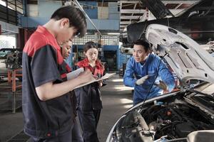 Asian male professional automotive engineer supervisor describes car engine maintenance and repair work with mechanic worker staffs team in fix service garage, specialist occupations in auto industry. photo