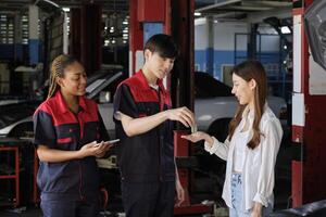 Asian female customer receives car key from automotive staff workers, quality guarantee with trust at maintenance garage, professional vehicle service center, ensuring fix checks, and repair industry. photo