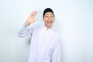 laughing asian muslim man waving hand show hi gesture isolated on white background photo