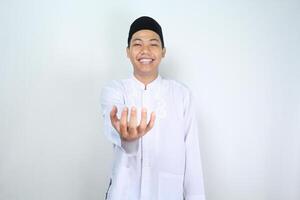 smiling asian muslim man showing empty palm at camera holding imaginary food plate isolated on white background photo