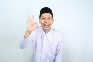 joyful asian muslim man show ok sign with laughing expression isolated on white background photo
