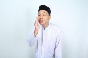 happy asian muslim man whispering something at camera isolated on white background photo