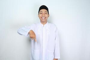 smiling muslim asian man looking at camera with pointing down below isolated on white background photo