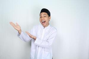 cheerful muslim asian man screaming while raising hand to presenting empty space isolated on white background photo